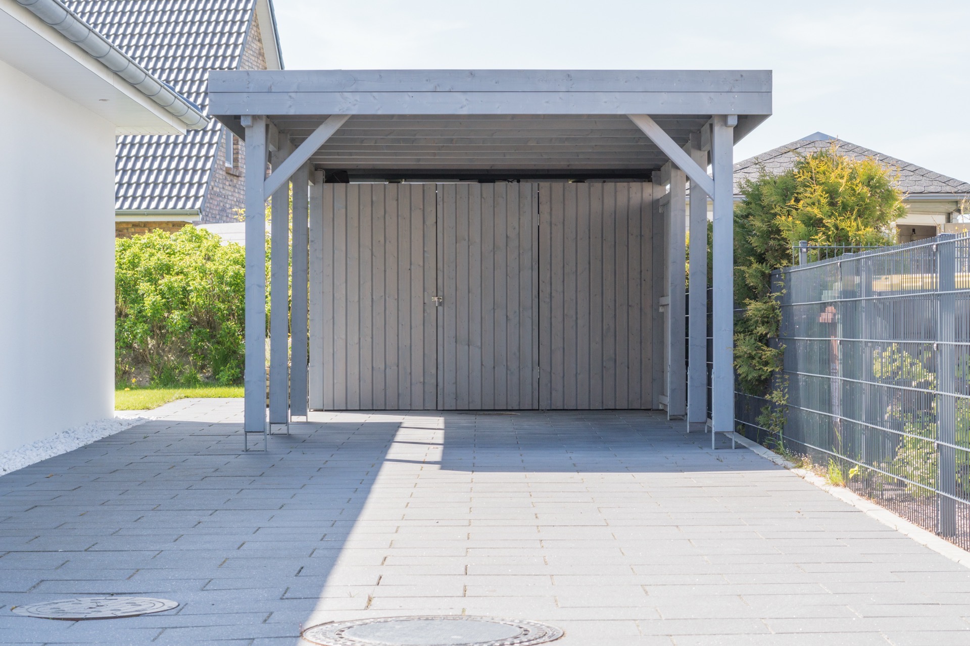 Fristående carport i gråmålat trä med stenlagd uppfart